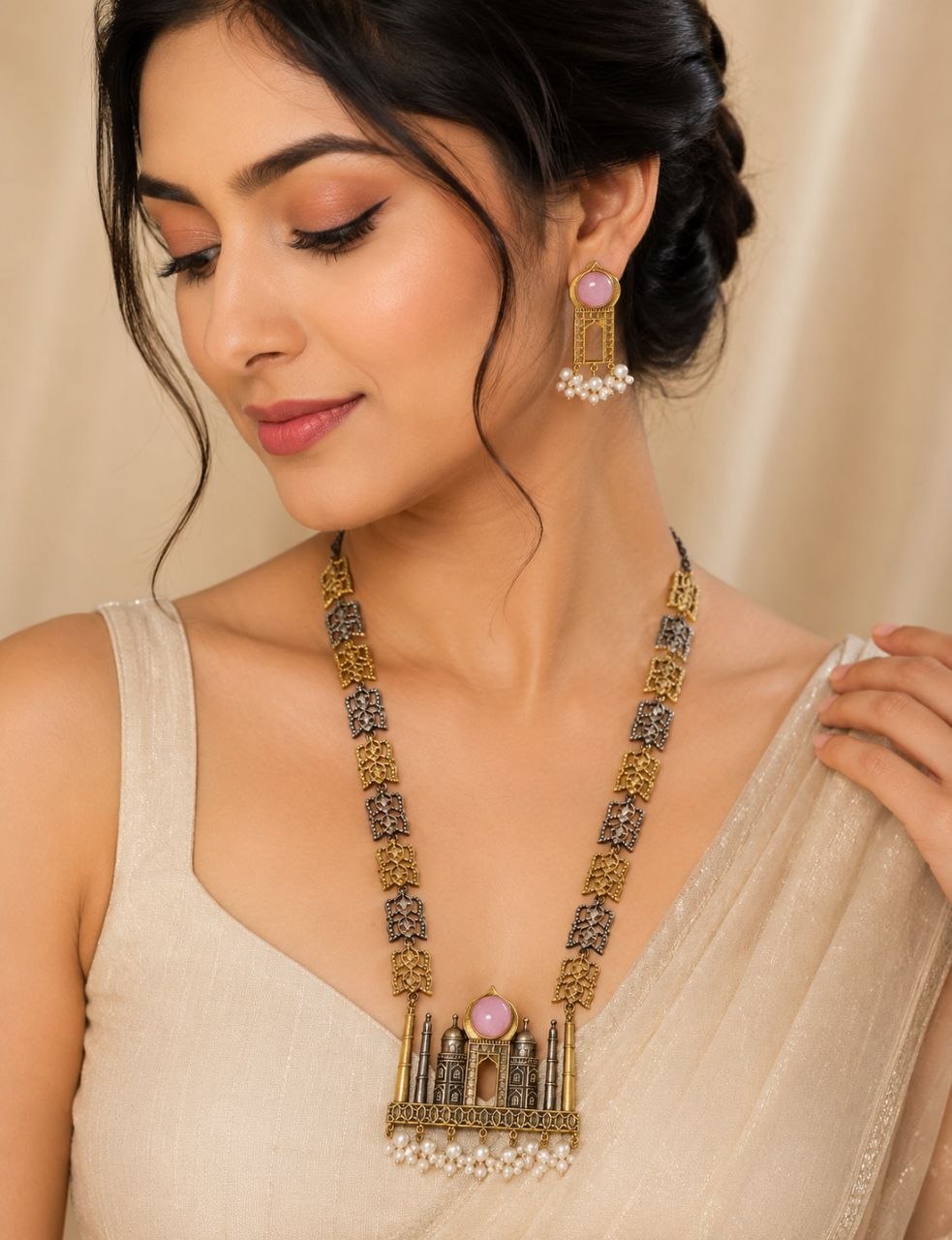 Antique gold and black Taj Mahal motif necklace with pink stone pendant and pearl drops alongside matching earrings on beige fabric with white flowers 2