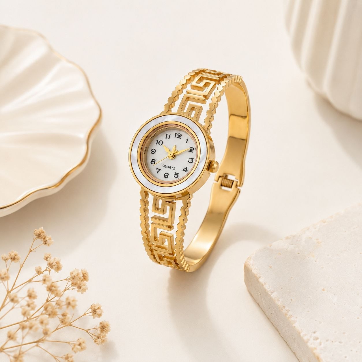 Gold women's bangle watch with intricate Greek key pattern on the band and luxurious mother-of-pearl dial featuring gold hands and markers 3