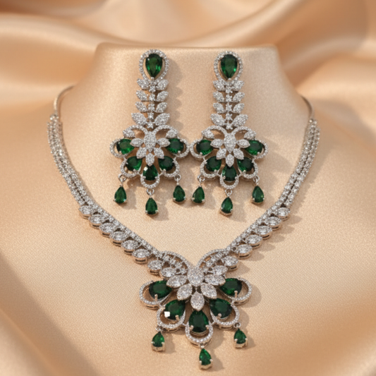 Emerald royal bloom necklace set with matching earrings featuring green pear-shaped stones and diamond detailing on satin background