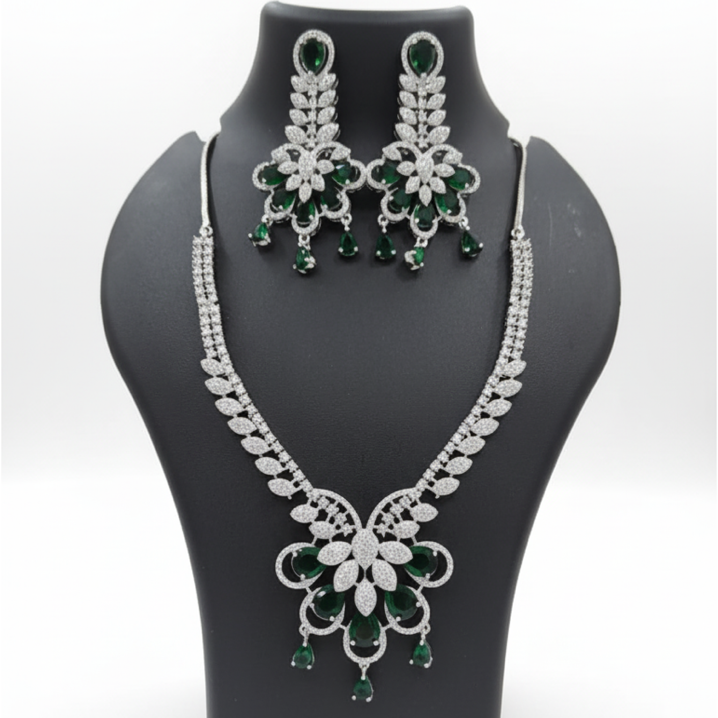 Emerald royal bloom necklace set with matching earrings featuring green pear-shaped stones and diamond detailing on satin background white