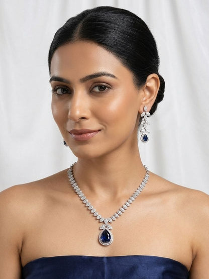 Silver necklace with large blue teardrop pendant surrounded by clear stones and matching leaf drop earrings on white fabric 2
