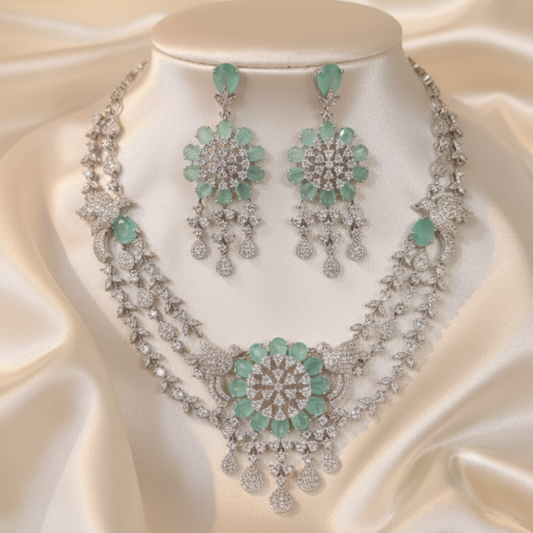 Aqua green double-layered necklace set with matching earrings featuring floral design and diamond detailing on black display