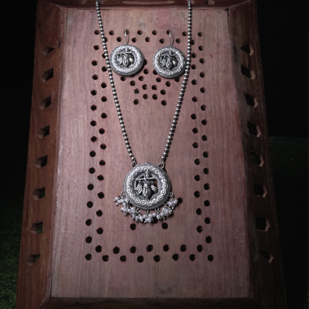 Revaaj Oxidized Silver Krishna Pendant Necklace with pearl accents, displayed on a wooden background.