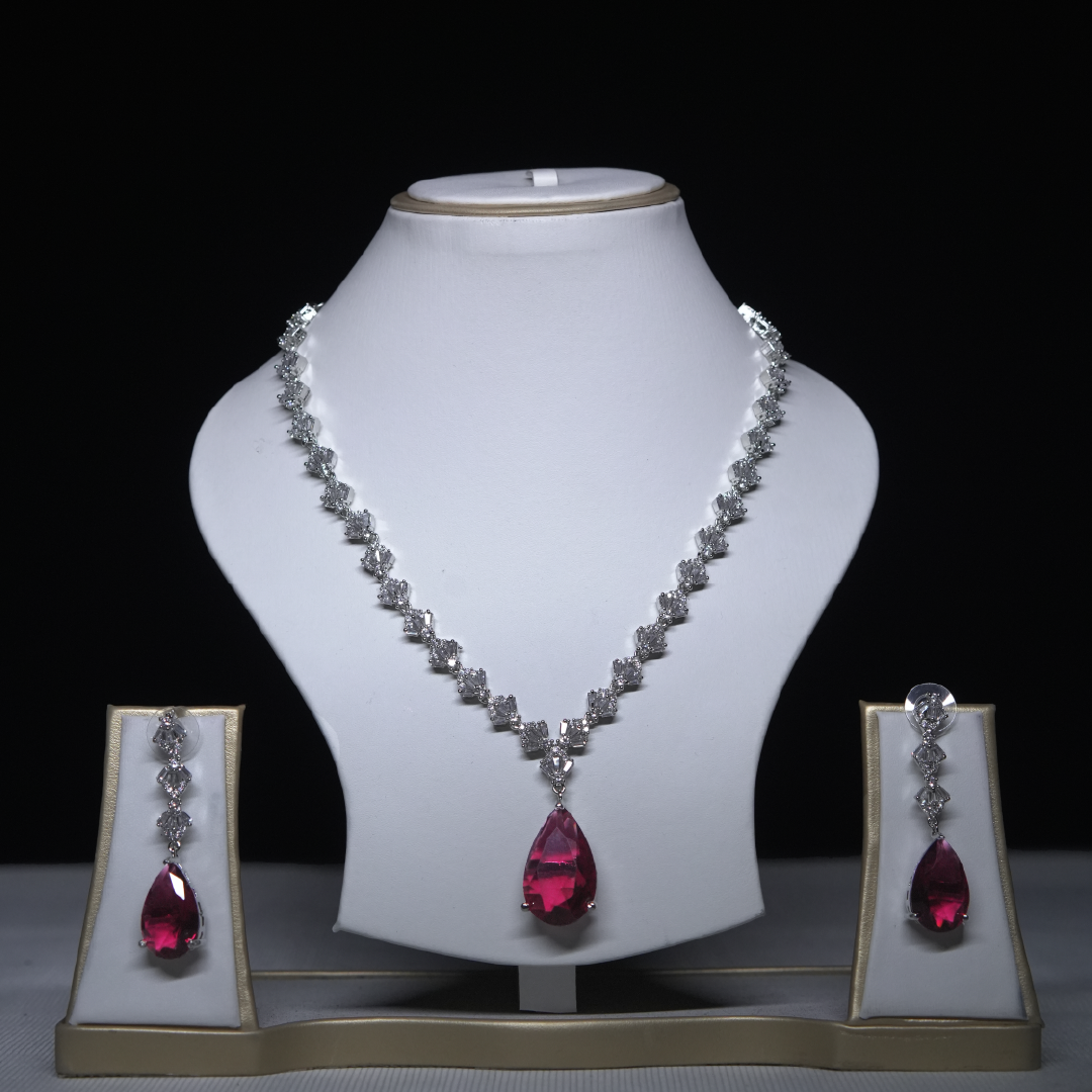 Revaaj Ruby and Cubic Zirconia Necklace and Earring Set displayed on a white stand against a black background.