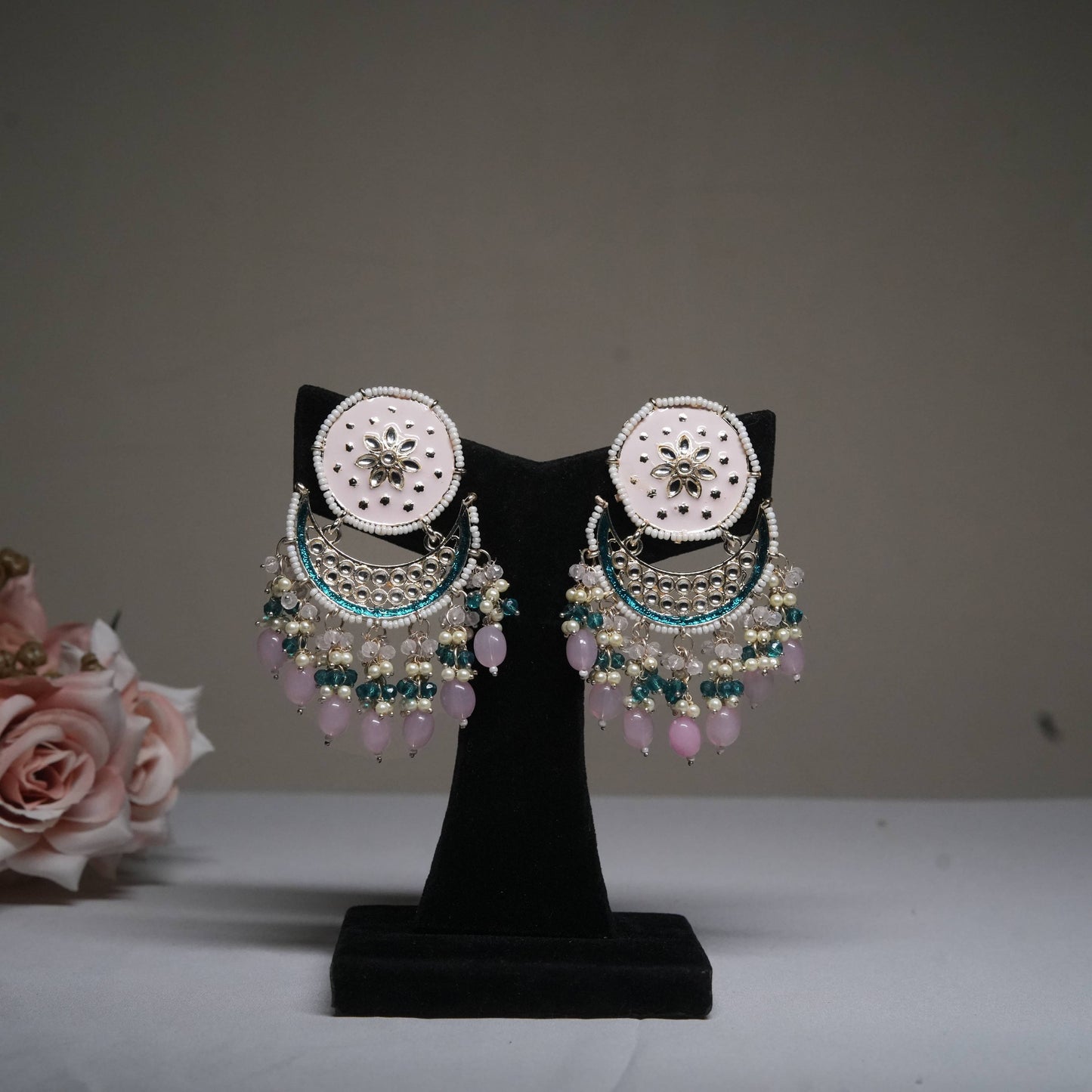 Pastel pink and blue chandbali earrings with pearl drops displayed on a black velvet stand.
