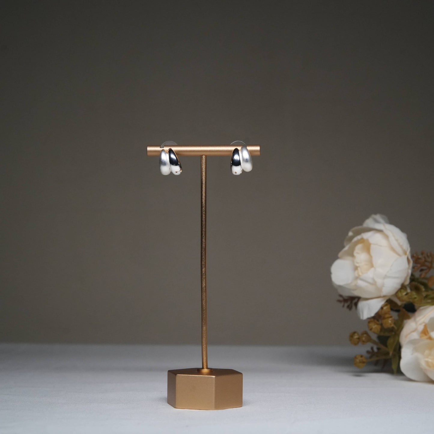 Minimalist silver hoop earrings in glossy finish displayed on a golden stand.