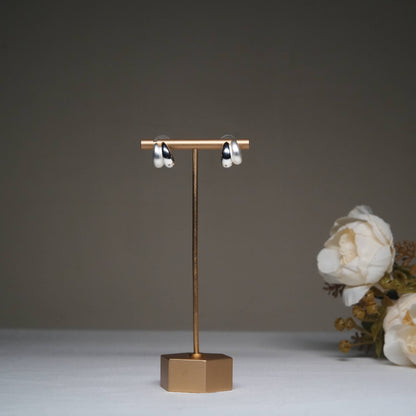 Minimalist silver hoop earrings in glossy finish displayed on a golden stand.