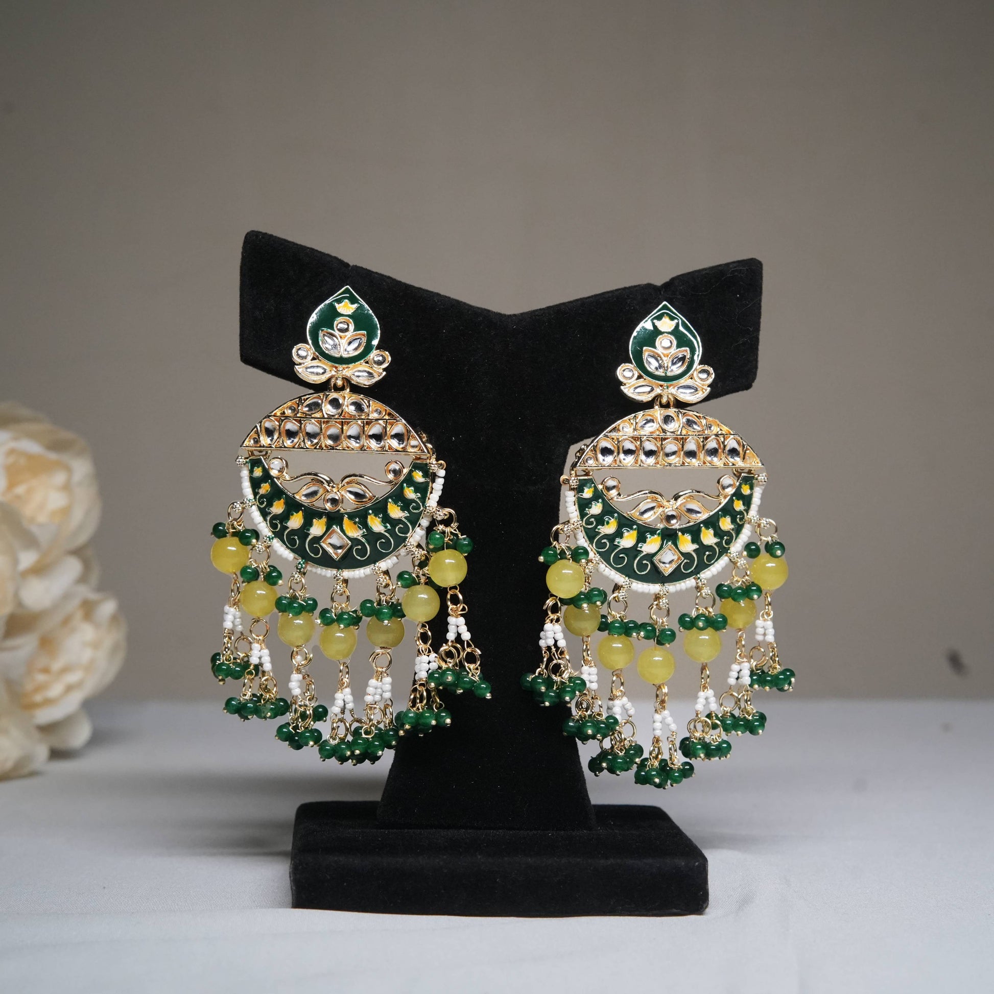 Green and yellow enamel chandbali earrings with pearl tassels displayed on a black velvet stand.