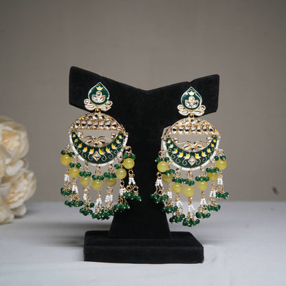Green and yellow enamel chandbali earrings with pearl tassels displayed on a black velvet stand.