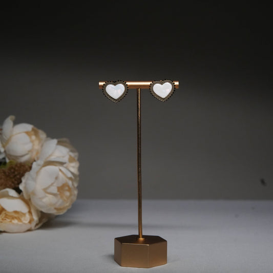 Classic white heart stud earrings with antique beaded detailing displayed on a golden stand.