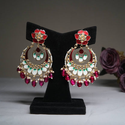 Enamel red and green chandbali earrings with ruby bead tassels displayed on a black velvet stand.