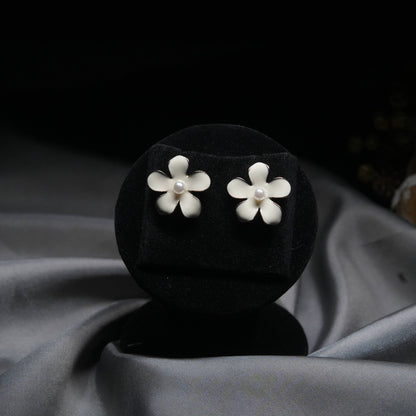 White enamel floral stud earrings with pearl center displayed on black velvet stand.